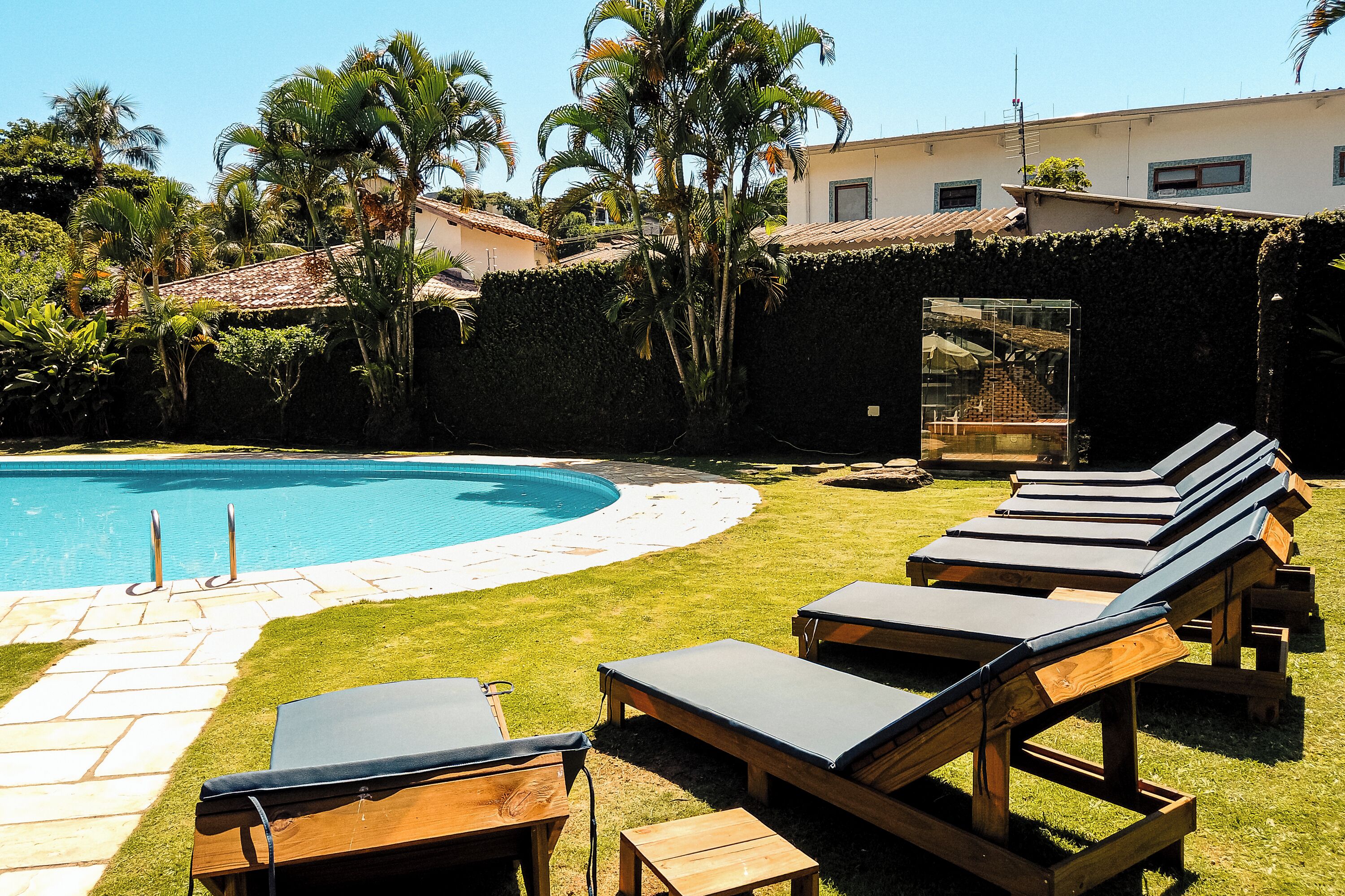 Uma piscina com espreguiçadeiras, um caminho de pedra e um edifício com telhado de azulejos.