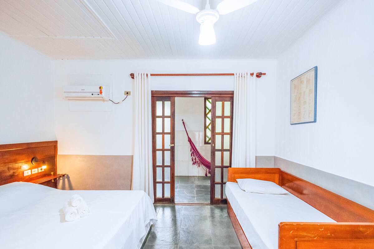 Habitación de hotel con dos camas individuales, ventilador de techo, ventana con cortinas, puerta con vistas y aire acondicionado instalado en la pared.