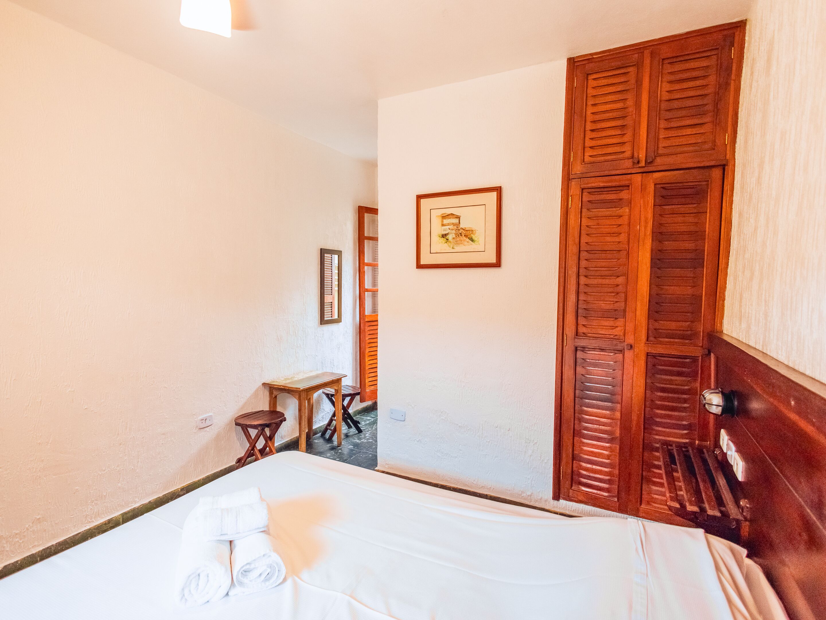 Habitació d'hotel amb un llit, una porta de fusta, una taula petita i un quadre a la paret.