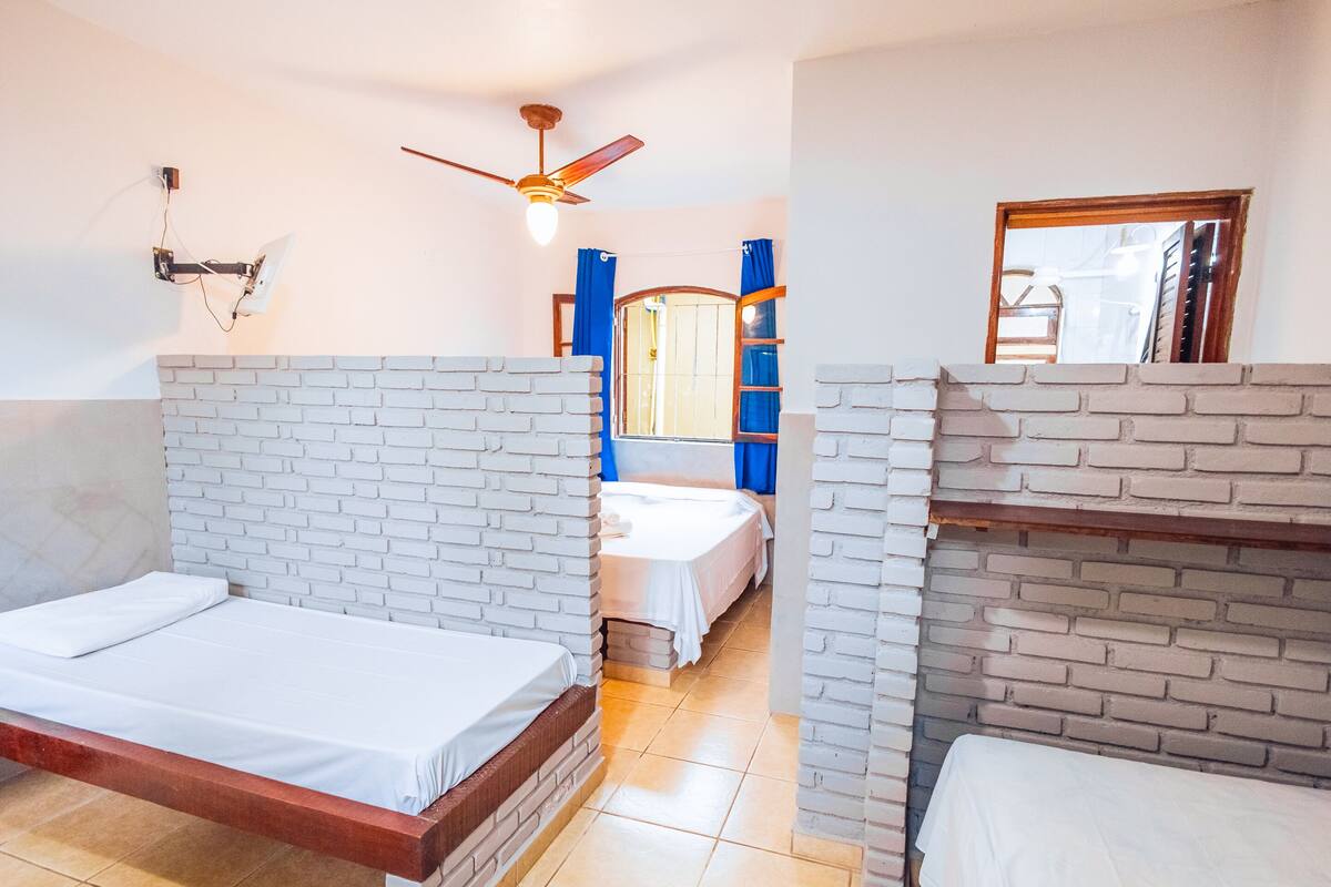Una habitación con dos camas, ventilador de techo, espejo y ventana con cortinas.