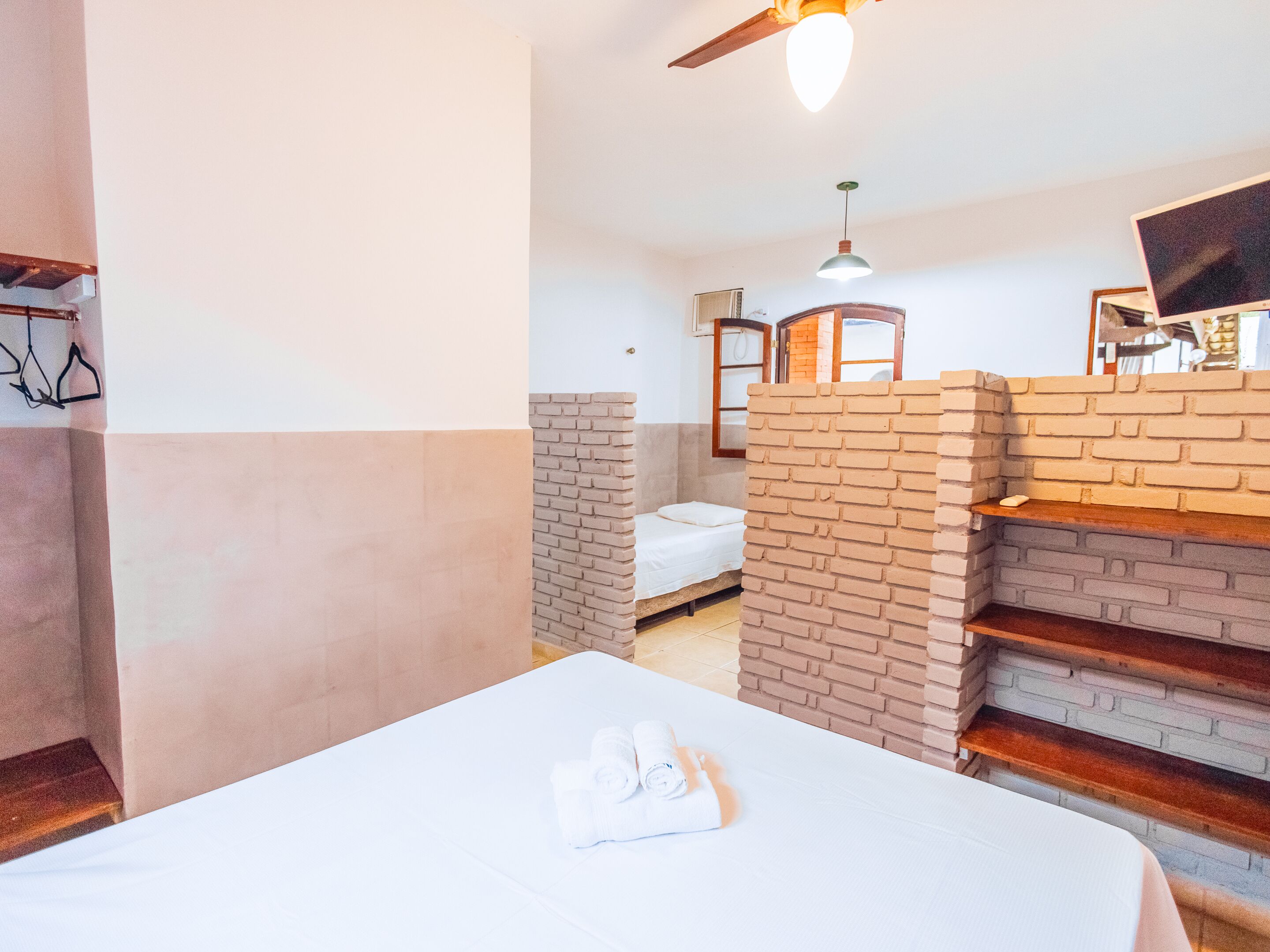 A hotel room with a bed, a brick accent wall, a ceiling fan, and a TV.