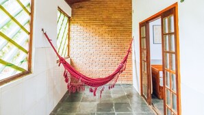 Un pasillo con una hamaca roja, piso de baldosas, techo de madera y pared de ladrillo.