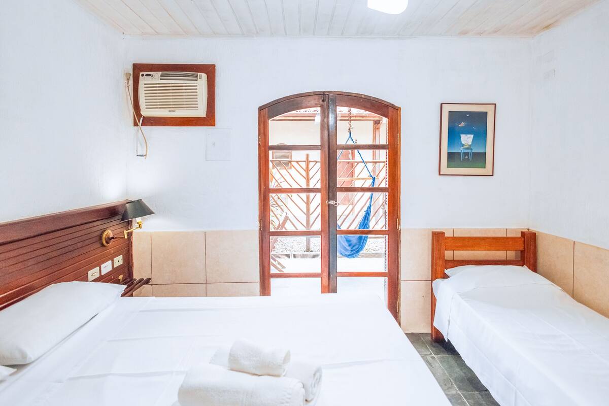 Una habitación con dos camas, un ventilador de techo, una puerta con vistas y un cuadro en la pared.