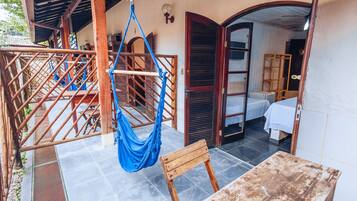 A room with a hammock, a wooden table, and a bed with a white sheet.
