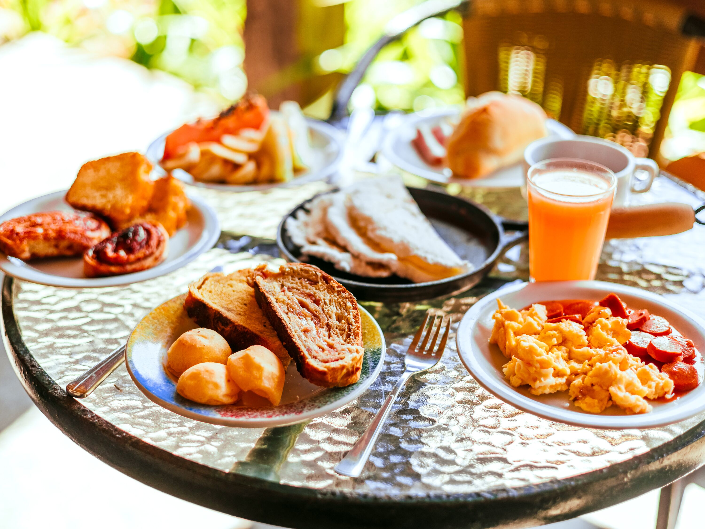 Mesa de café da manhã com torradas, ovos mexidos, linguiça e um copo de suco de laranja.