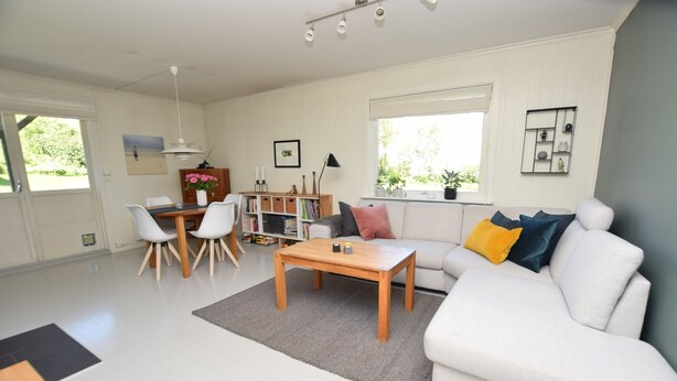 A spacious living room with a white sofa, a wooden coffee table, and a dining area with a white table and chairs. - Solferie Apartment Odins Gate (Kristiansand)