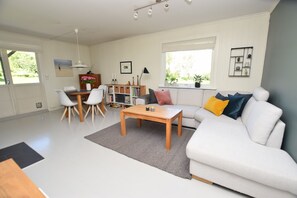 A spacious living room with a white sofa, a wooden coffee table, and a dining area with a white table and chairs. - Solferie Apartment Odins Gate (Kristiansand)