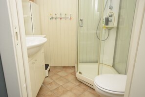 Un baño con ducha de mampara de vidrio, un lavamanos blanco y un inodoro.