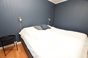 Un dormitorio con una cama, dos lámparas de noche, una mesita y una planta.
