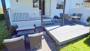 A covered outdoor patio with a wooden deck, wicker furniture, and a barbecue grill. - Solferie Apartment Odins Gate (Kristiansand)