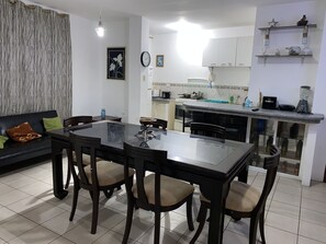 A modern living room with a dining table and chairs, a sofa, and a kitchen area with cabinets and appliances. - Playa Suites Apart-Hotel (Manta)