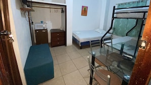 Una habitación pequeña con una litera, un escritorio, una silla, un armario y un microondas.
