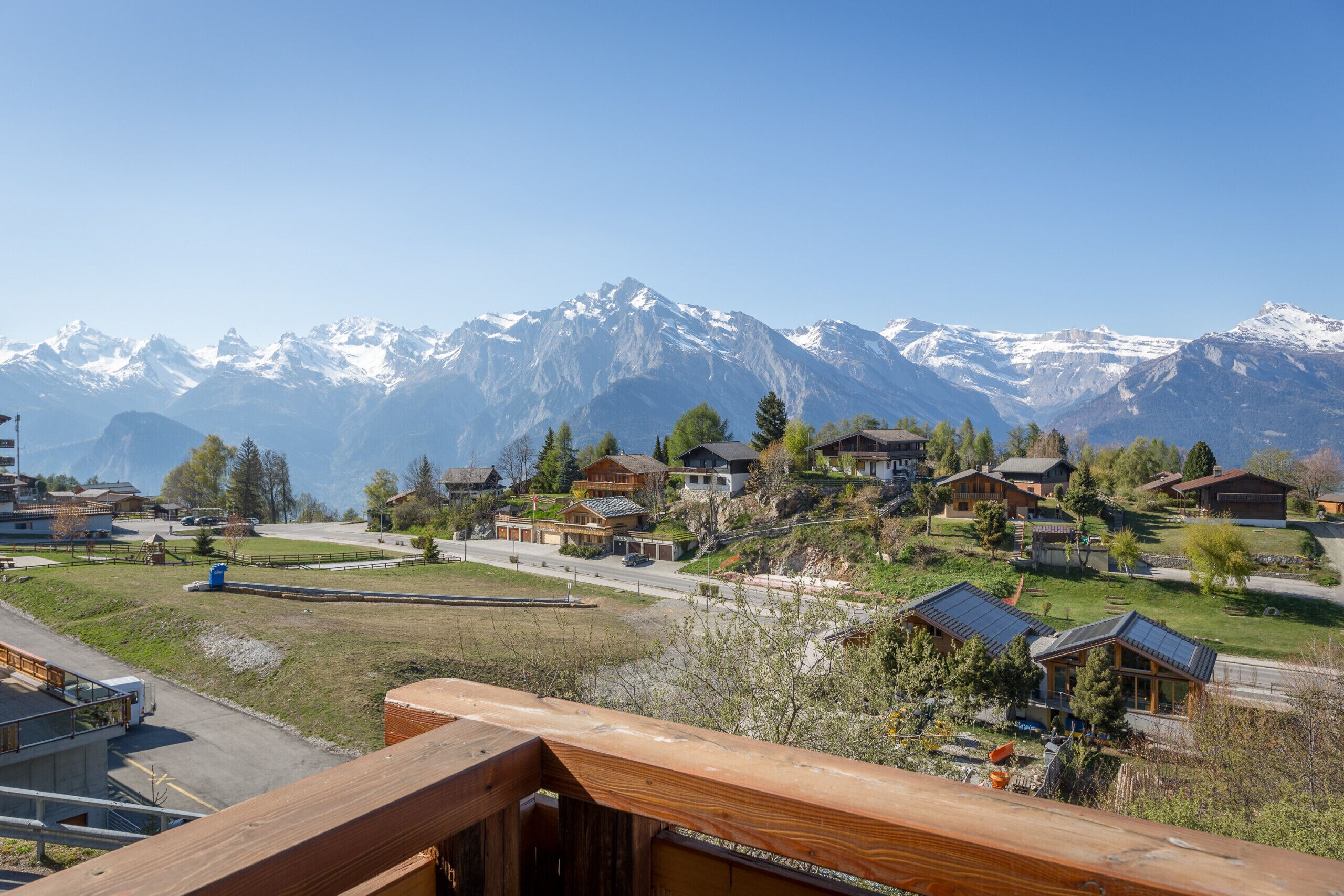 A residential area with houses on a hillside, a road, and snow-capped mountains in the background.