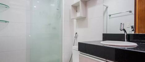 A modern bathroom with a glass shower enclosure, a white toilet, a black countertop with a sink, and a mirror above the sink.