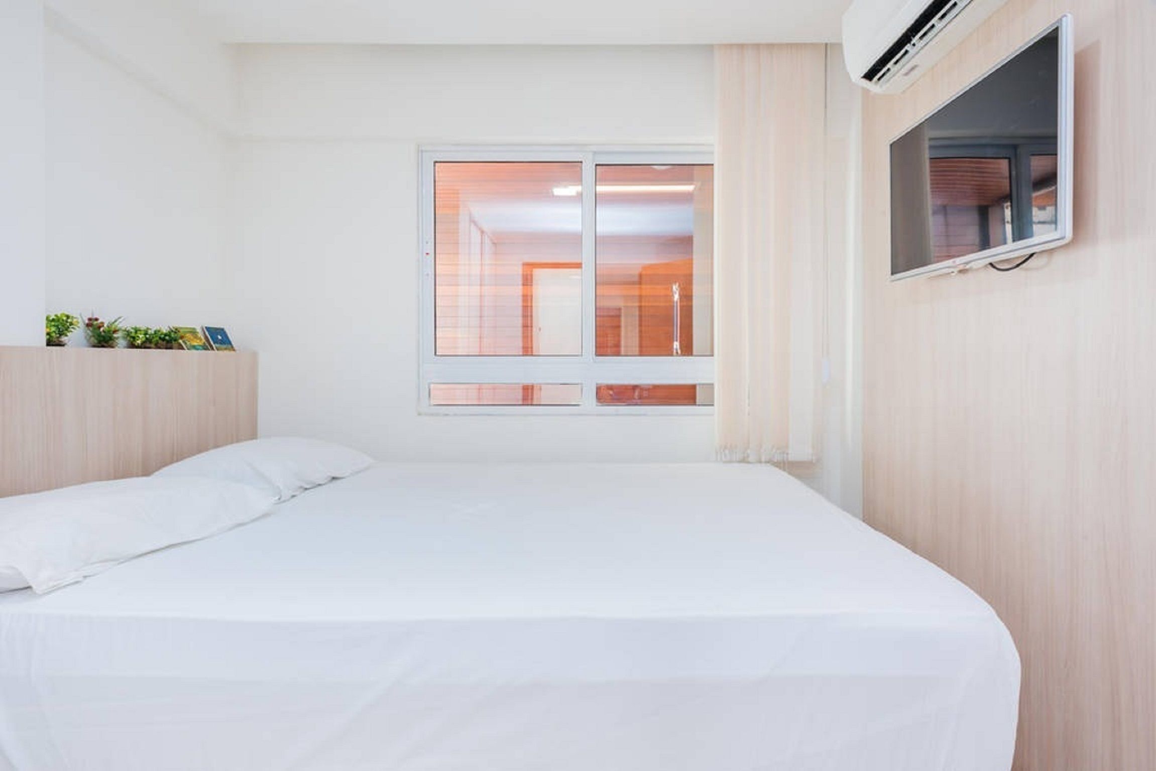 A bedroom with a bed, a window, and a mounted TV.
