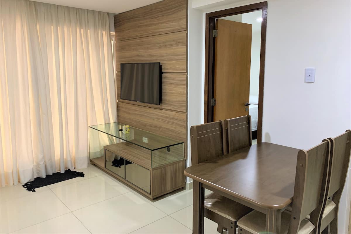 Una sala de estar moderna con una mesa de centro de vidrio, un aparador de madera y un televisor montado en la pared.