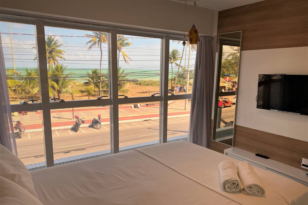 Habitación de hotel con un amplio ventanal que ofrece vistas a palmeras y una carretera con motocicletas.