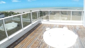 A balcony with a wooden deck, a hot tub, and a view of the beach and ocean.
