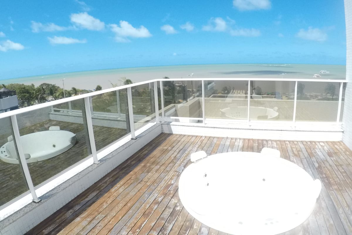 Un balcón con terraza de madera, un jacuzzi y vistas a la playa y al océano.