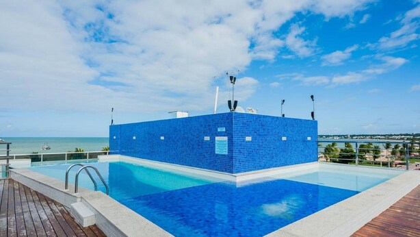 A rectangular swimming pool with a blue tiled deck, surrounded by a wooden deck and a metal railing.