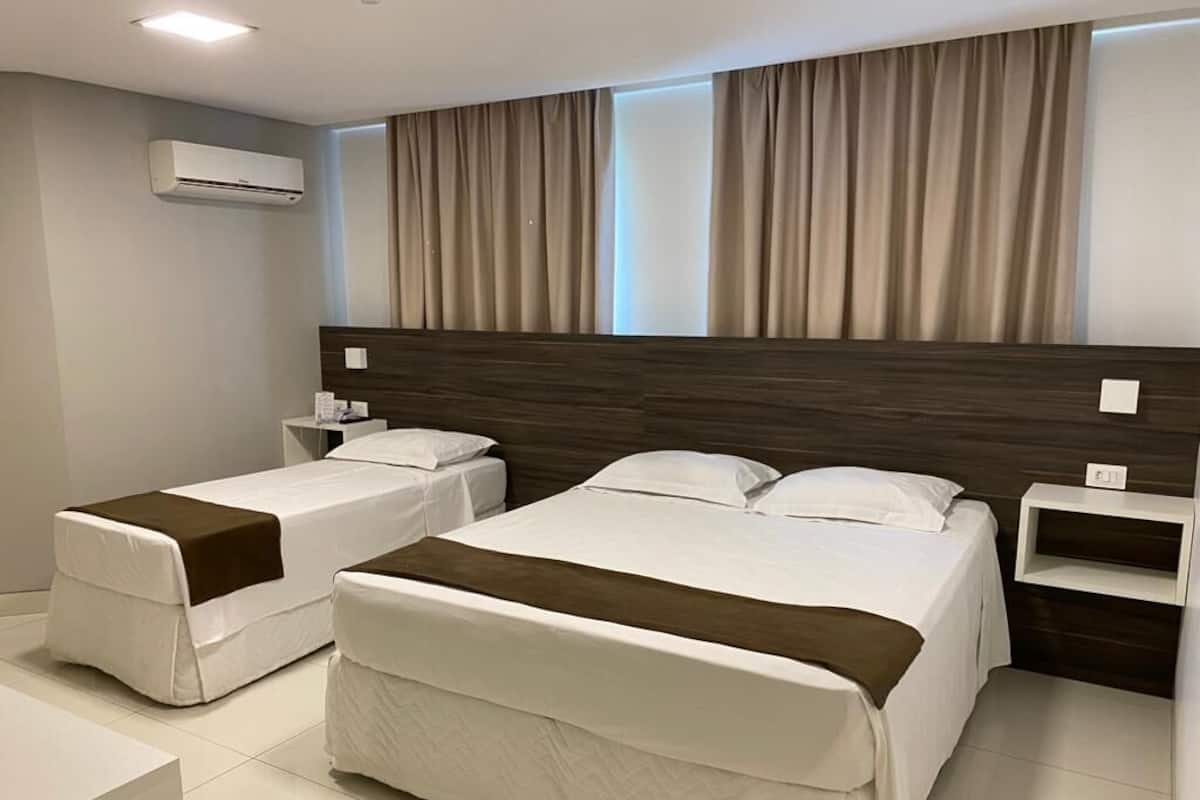 A hotel room with two beds, a bedside table, a nightstand, and an air conditioning unit.