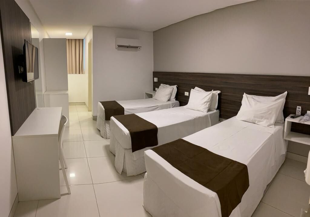 A hotel room with three single beds, a desk, and a TV.