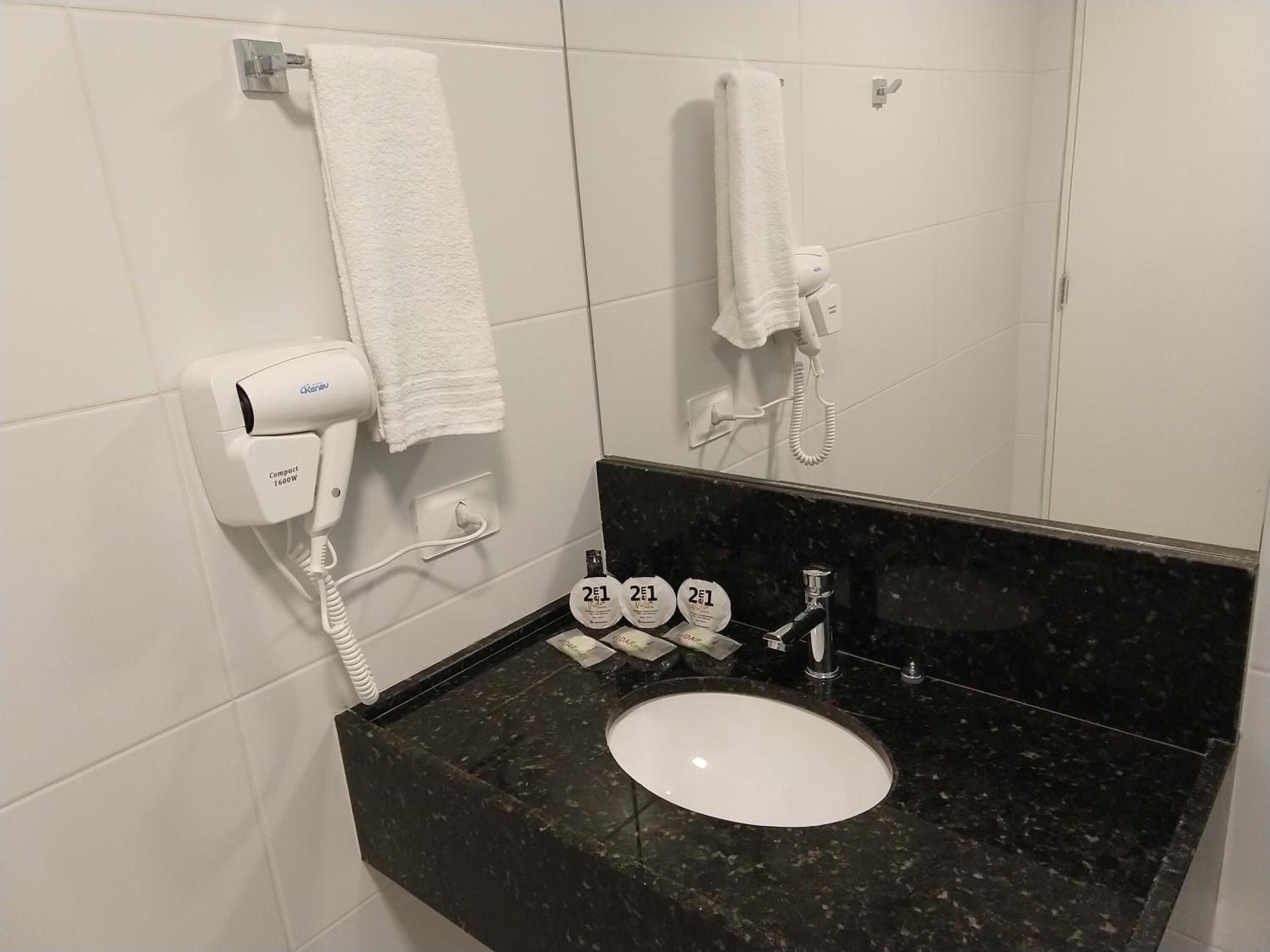 A bathroom with a white sink, black marble countertop, a hairdryer, and two bottles of hand soap.