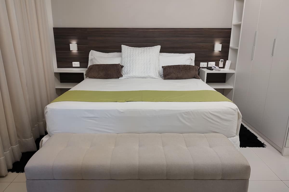 A neatly arranged hotel room with a large bed, a bedside table, a nightstand, and a wardrobe.
