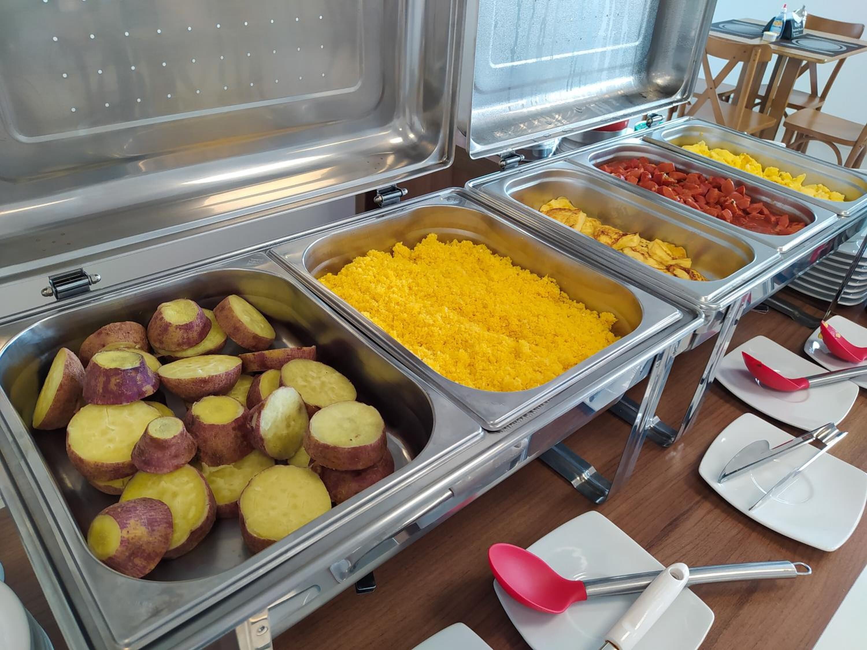 A buffet with various food items including sliced potatoes, yellow rice, and diced tomatoes.