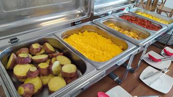 A buffet with various food items including sliced potatoes, yellow rice, and diced tomatoes.