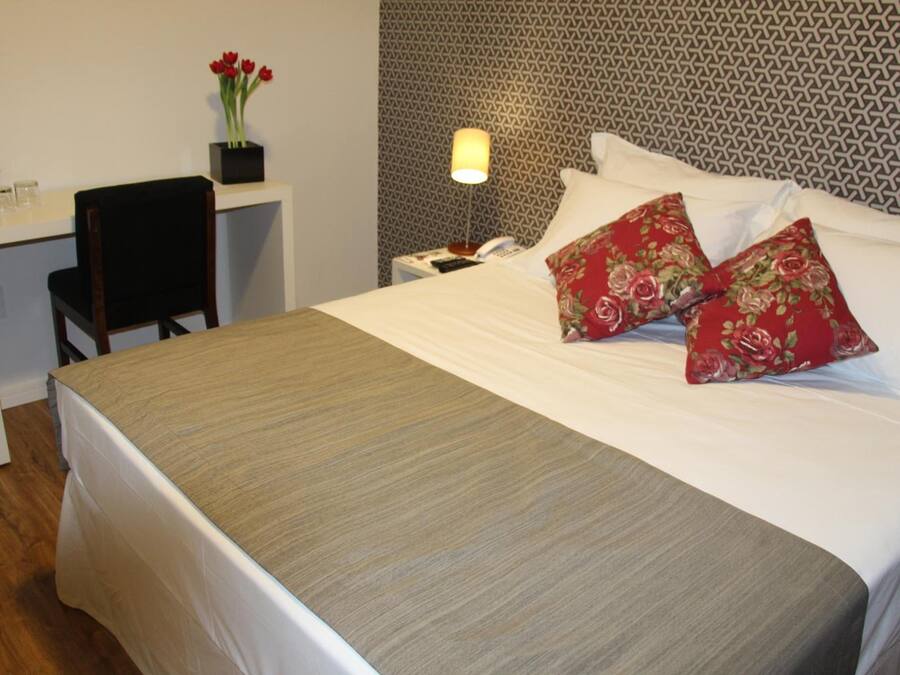 A neatly made bed with a patterned headboard, a bedside table with a lamp, and a chair.