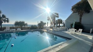 A swimming pool with lounge chairs and umbrellas, a clear sky, and a palm tree.