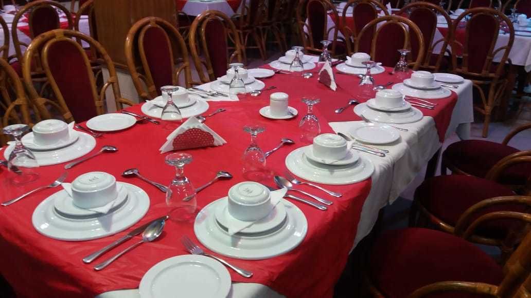 Un salón de banquetes con mesas dispuestas para un evento formal, con manteles blancos y sillas rojas.