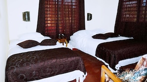 Habitación de hotel con dos camas, cortinas oscuras y una mesita con una botella y vasos.