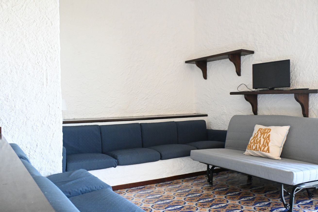 A room with a blue sofa, a grey sofa, a patterned floor, and a TV on a shelf.