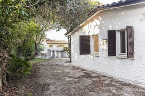 A white building with brown shutters, a stone pathway, and a gate leading to a courtyard.