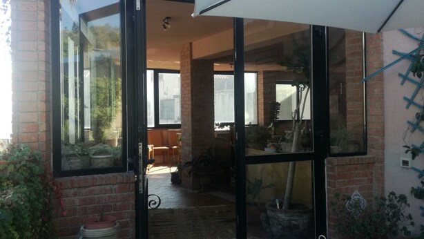 Une entrée avec une porte en verre, un parasol blanc, des plantes en pot et une terrasse carrelée.