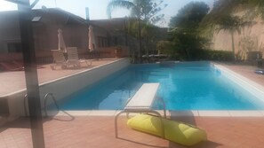 A swimming pool with a sunshade, lounge chairs, and a yellow flotation device. - Villa Grande (Messina)