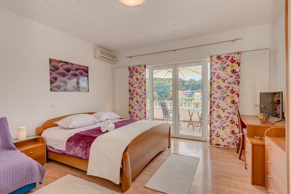 A bedroom with a bed, a dresser, a chair, and a balcony with a view of the outdoors.