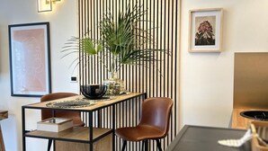 Un salón moderno con suelo de madera, una mesa de metal negro, un sillón de cuero marrón, una planta en maceta y un panel de pared a rayas.