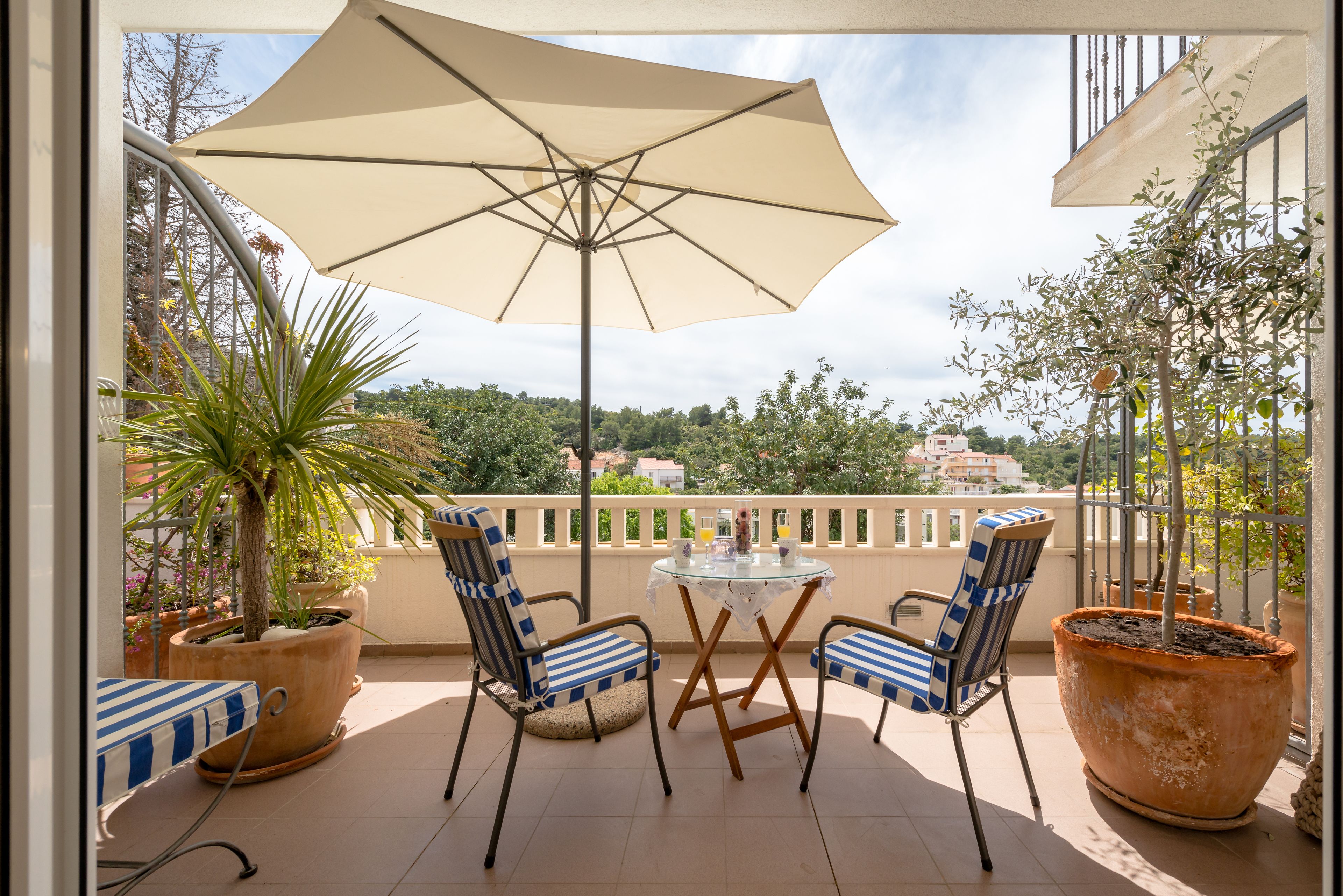 Uma varanda com duas cadeiras, uma mesa e um grande guarda-sol.