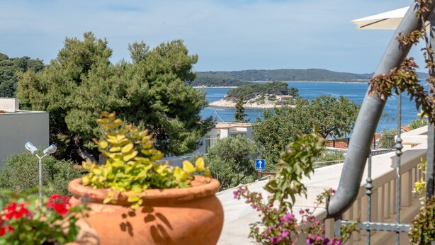 Una terraza con vista al mar, plantas en macetas y un letrero azul que indica una dirección.