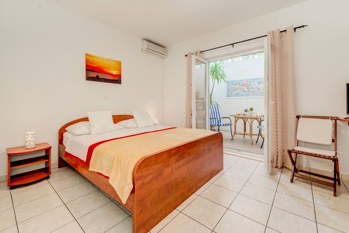 A bedroom with a wooden bed, a nightstand, a chair, and a view of the outdoors.