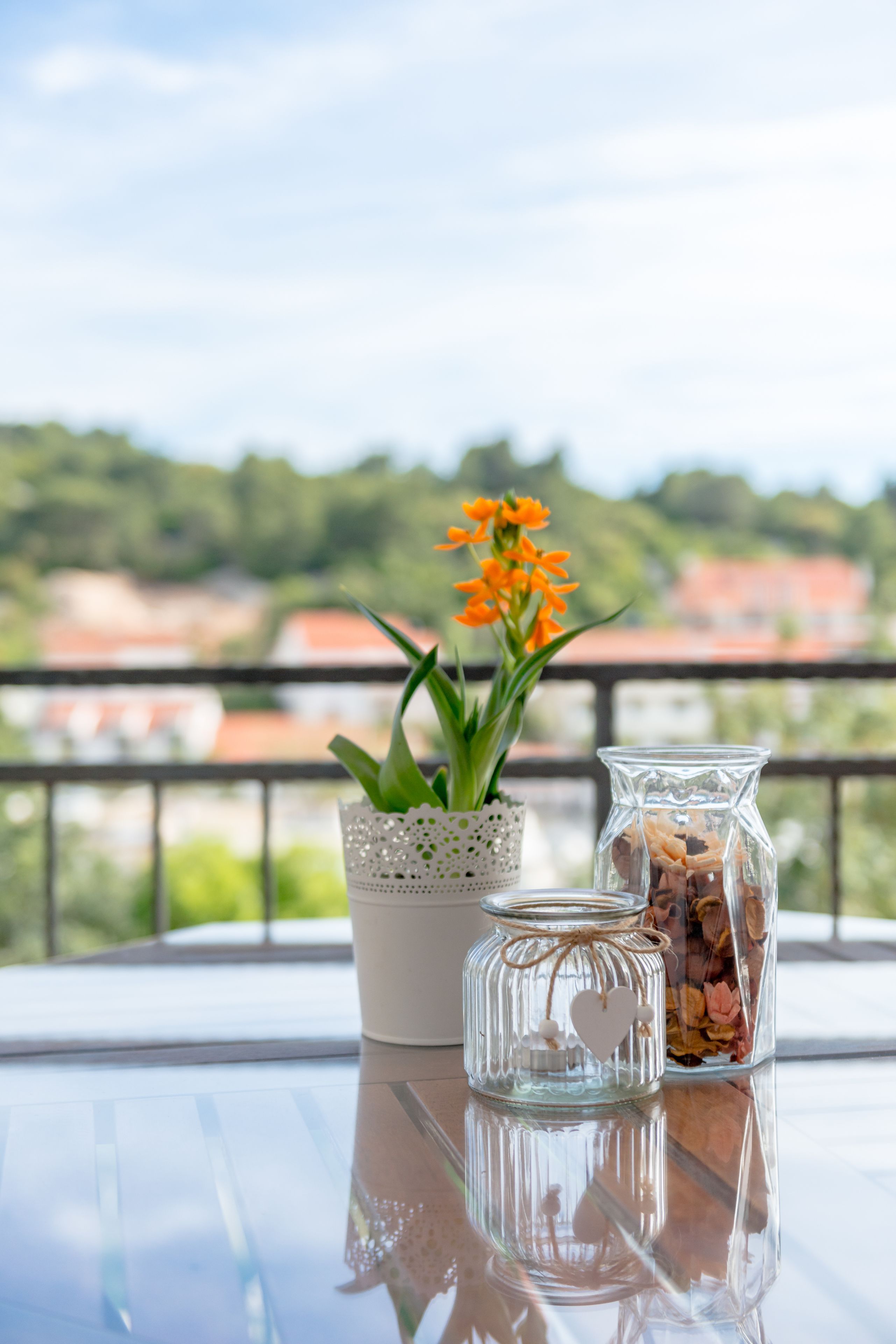 A balcony with a table displaying a potted plant and a glass jar with dried flowers.