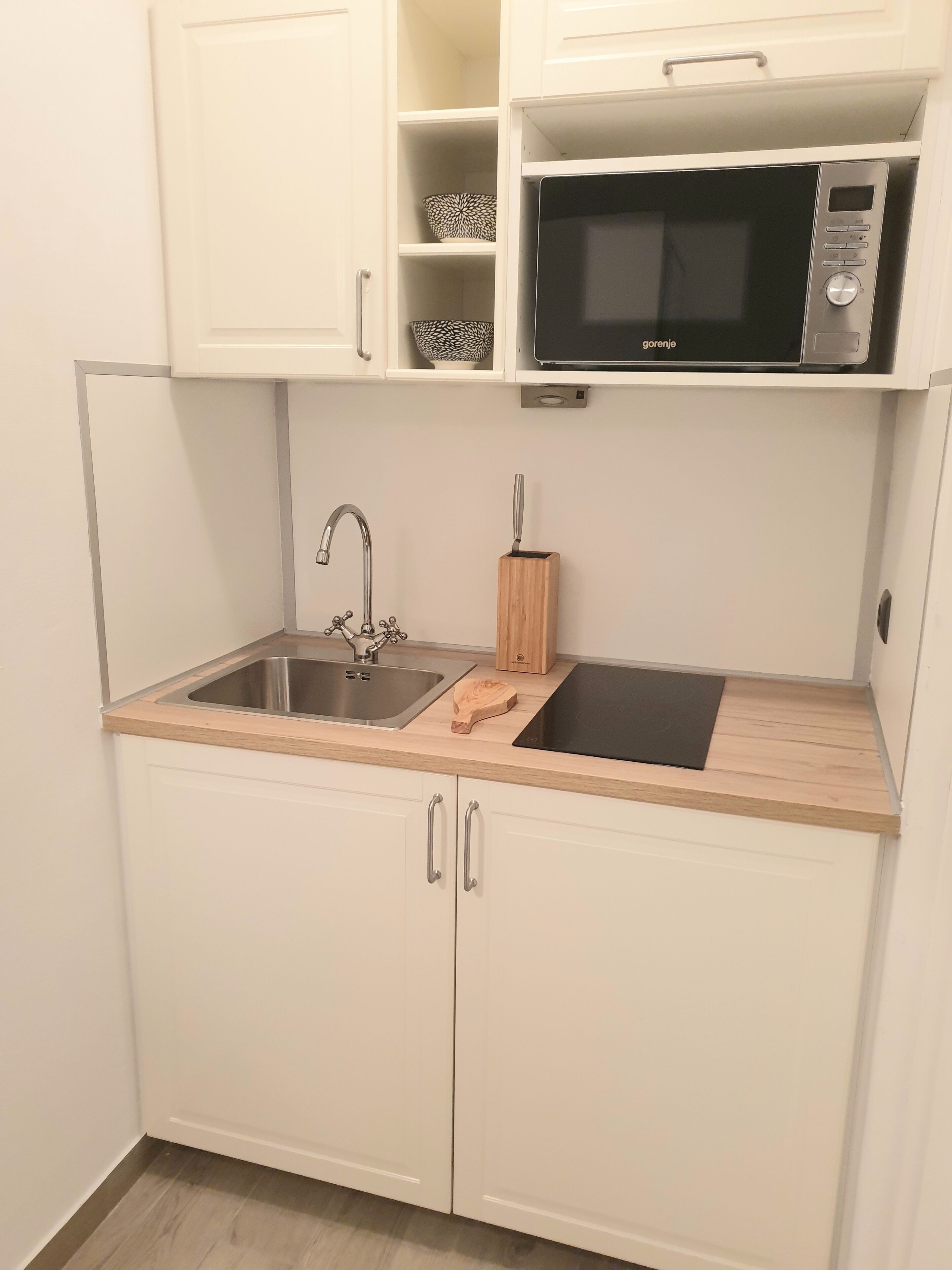 A compact kitchen with a sink, a microwave, and white cabinets.