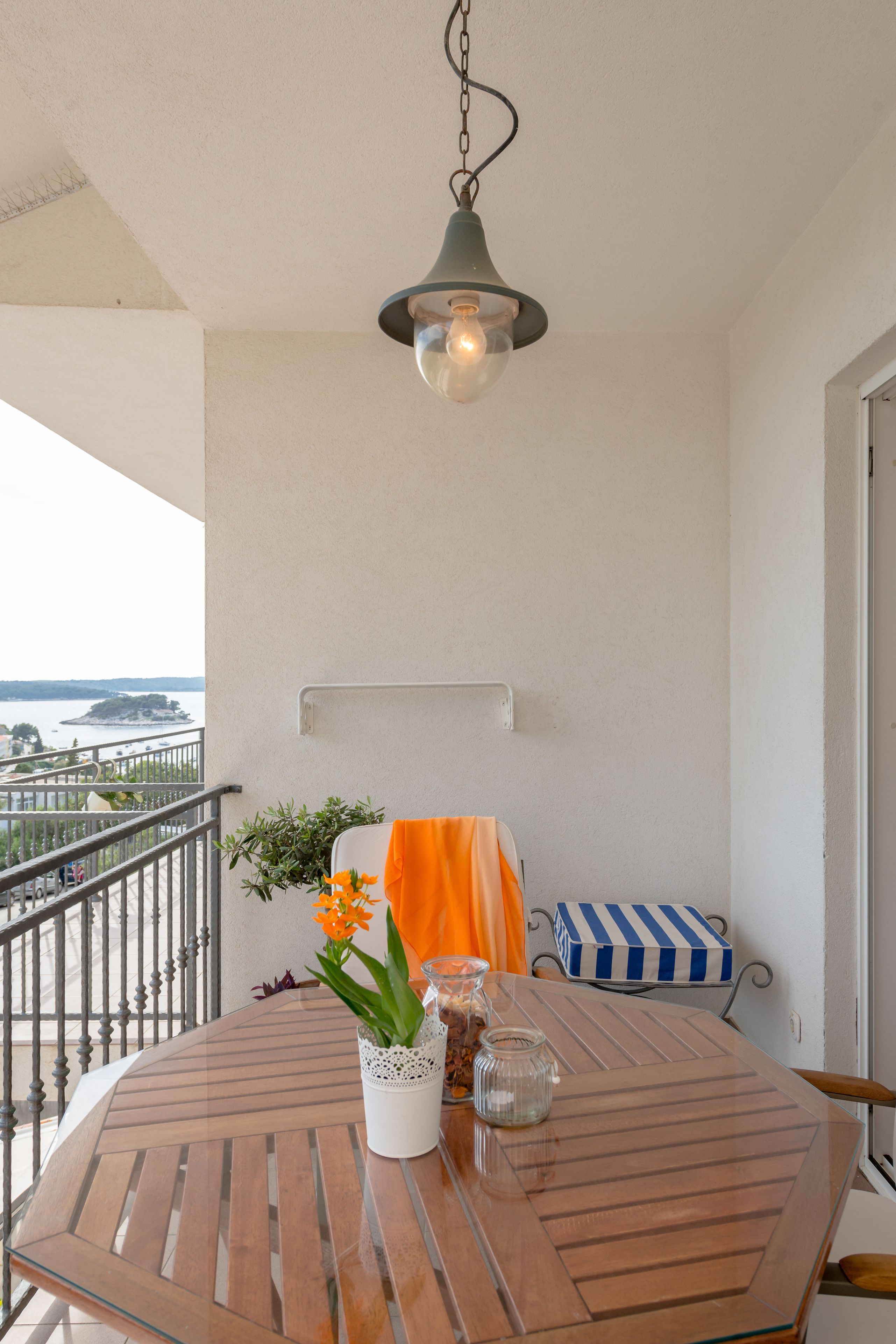Un balcón con una mesa redonda de madera, una lámpara colgante y vistas al mar.