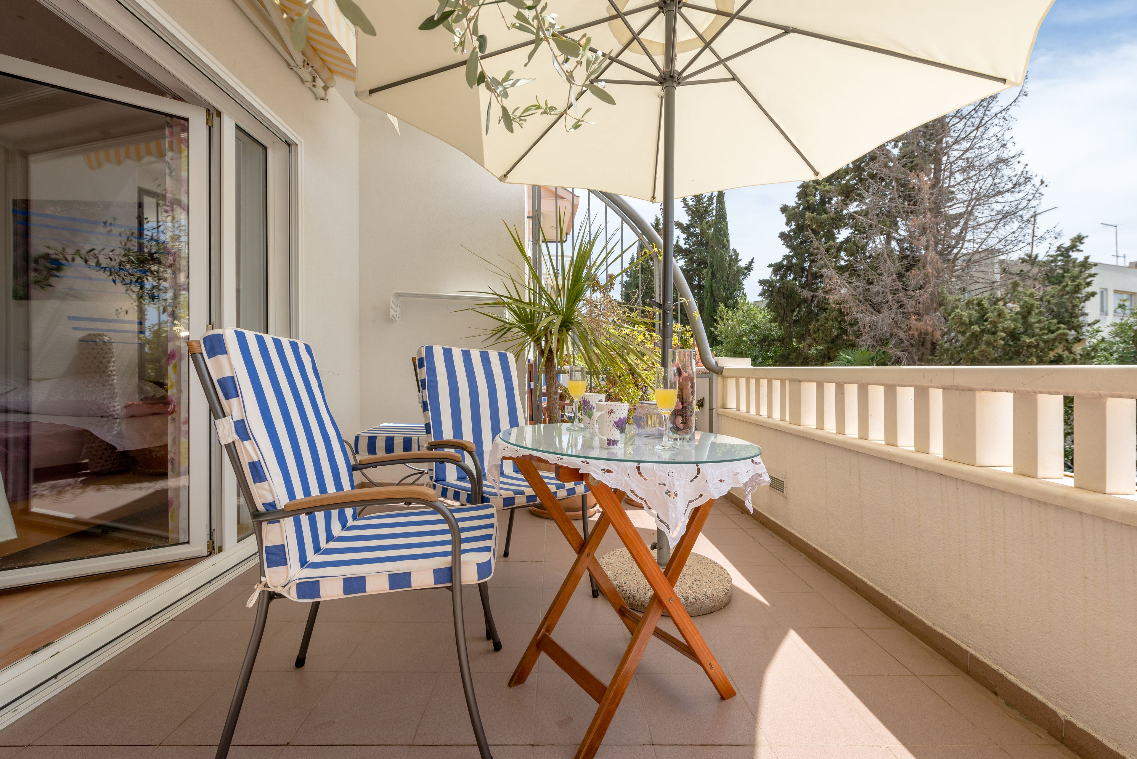 A balcony with two striped chairs, a glass table, and a large umbrella.