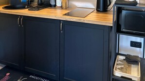 Una cocina moderna con encimera de madera, armarios negros y salpicadero negro. Hay repisas sobre la encimera con diversos utensilios de cocina y plantas.