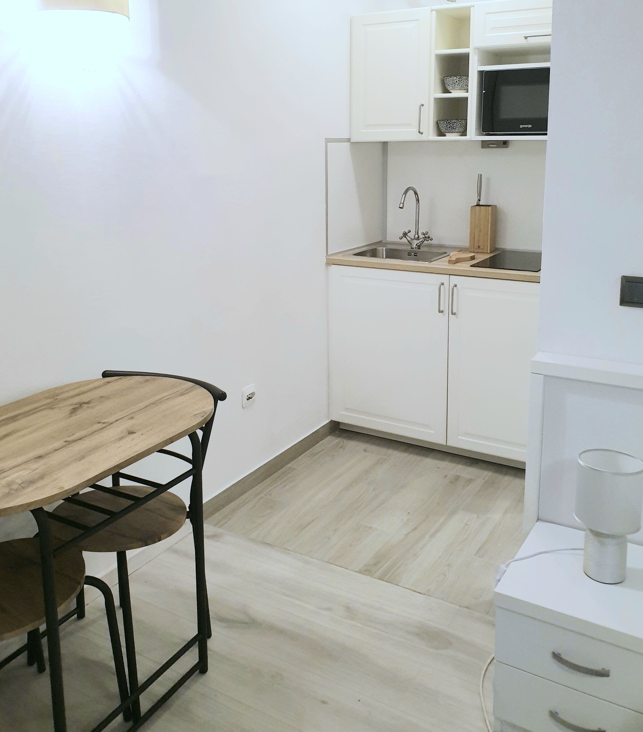 A small kitchen with white cabinets, a wooden table, and a microwave.