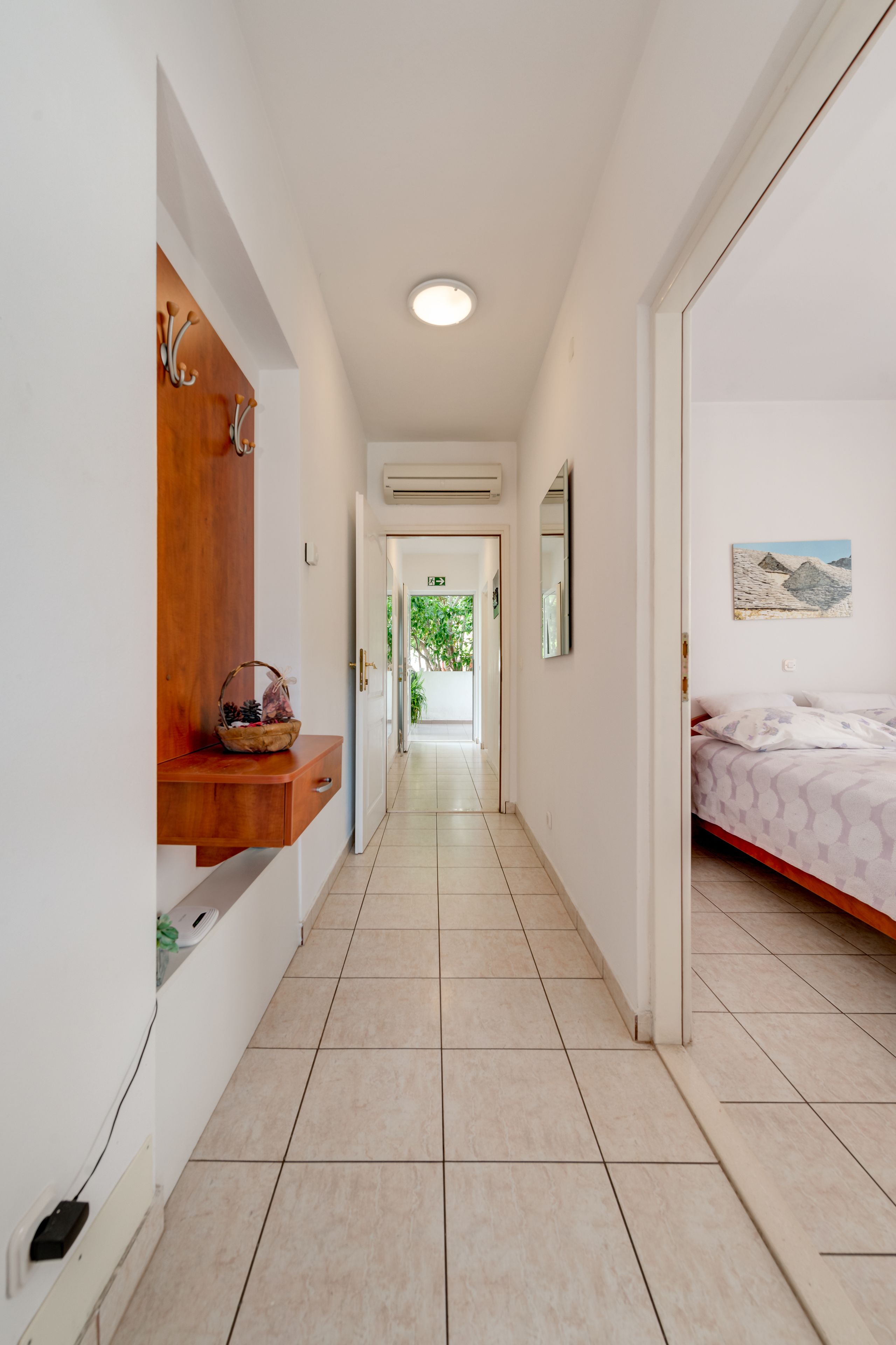 A hotel corridor with a wooden shelf, a bed with patterned bedding, and a painting on the wall.